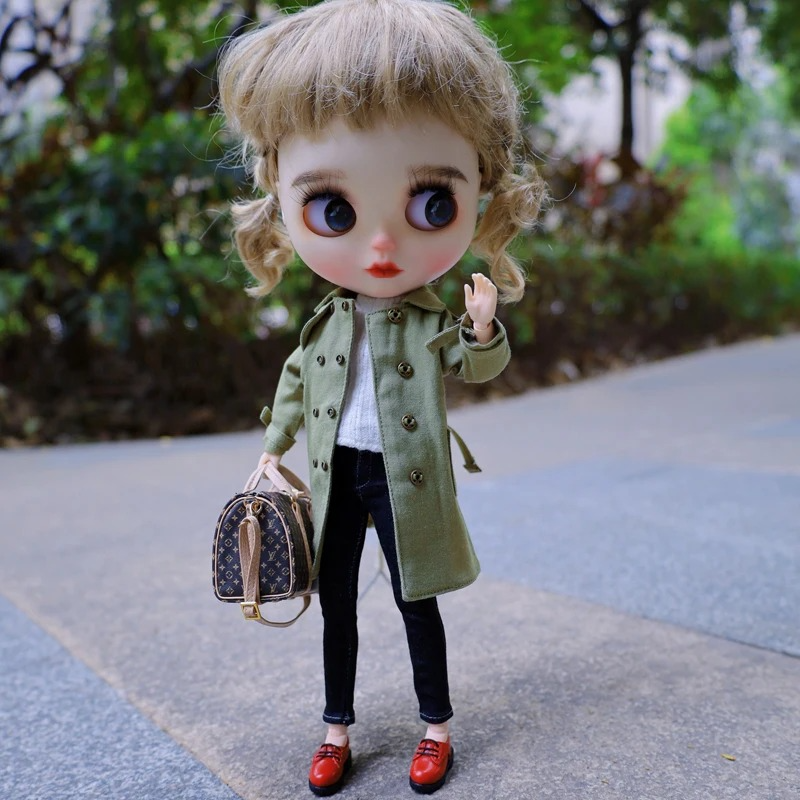 Neo Blythe doll wearing a green trench coat, black jeans, and red shoes, holding a small handbag.