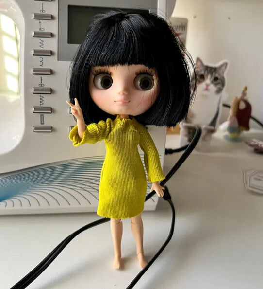 Middie Blythe Doll with short black hair in a yellow dress, standing beside a sewing machine and a cat.