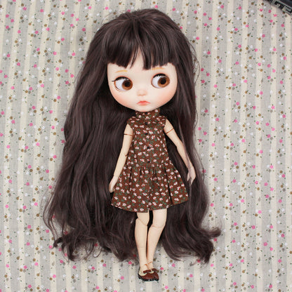 A Neo Blythe doll wearing a brown floral dress, showcasing long dark hair and an adorable expression on a patterned background.