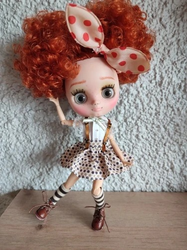 Middie Blythe doll with red afro hair, polka dot bow, and a cute outfit, standing on a wooden surface.
