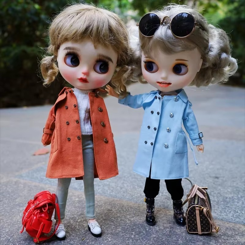 Two Neo Blythe dolls dressed in stylish trench coats, one orange and one blue, posing outdoors.