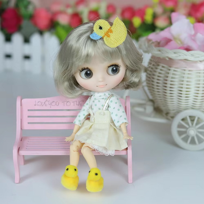 Middie Blythe doll with short blonde hair, dressed in a polka dot top and yellow shoes, sitting on a pink bench.