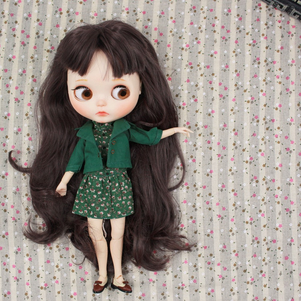 Neo Blythe doll wearing a stylish green jacket and dress combo with floral patterns, posed on a patterned background.