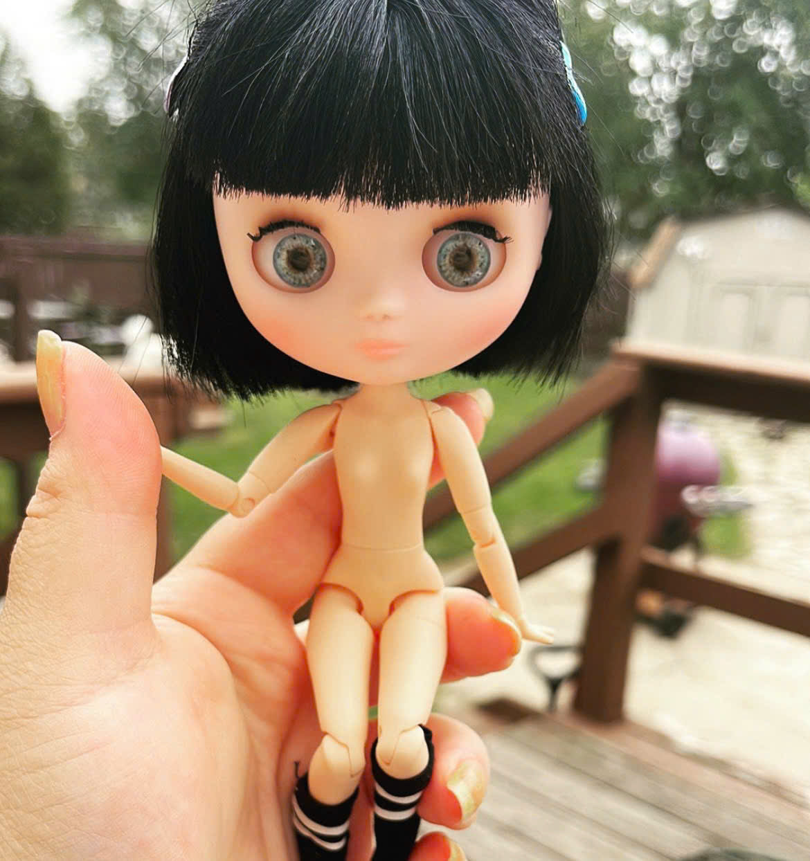 Middie Blythe Doll with short black hair and matte face held in hand, showcasing jointed body and expressive eyes.